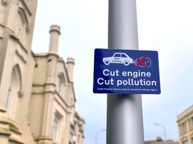 A picture of a sign on a lamppost - the sign reads "cut engine, cut pollution"