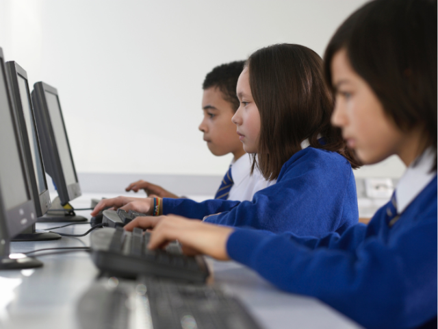 3 children in blue school uniform sitting at a desk working on computers