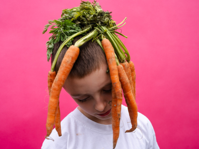 Picture of child with a bunch of carrots draped over their head!