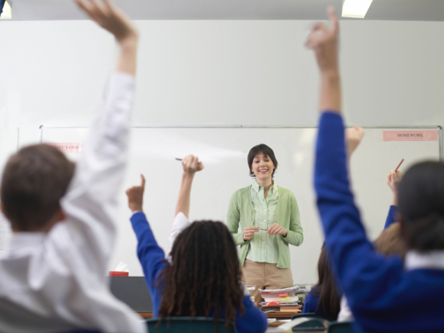 A photo of a group of school students with their hands raised