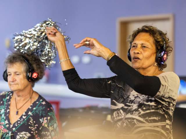 two ladies sitting down wearing headphones and one waving pompom 