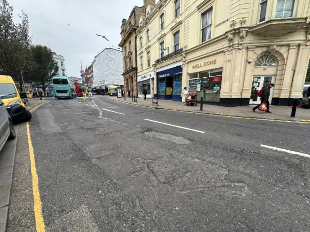 A picture of a road with potholes, shops and cars