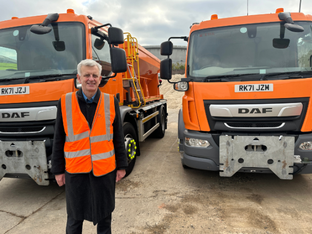 A man standing in front of two gritting lorries