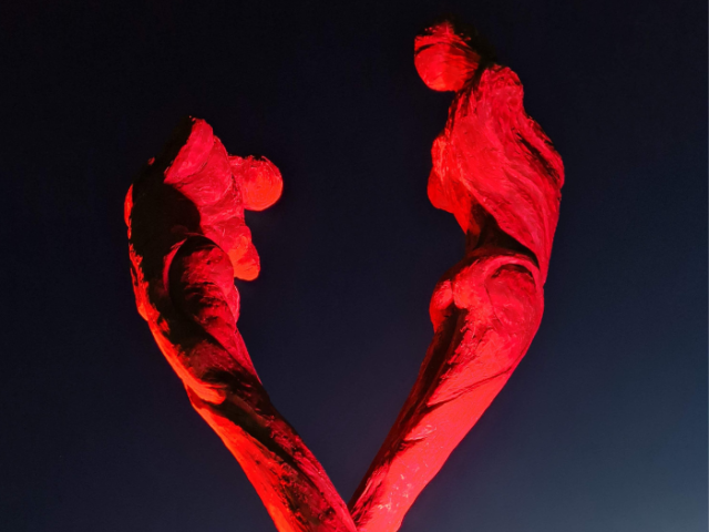 The image shows the Brighton AIDS Memorial statue at night, lit up in red.