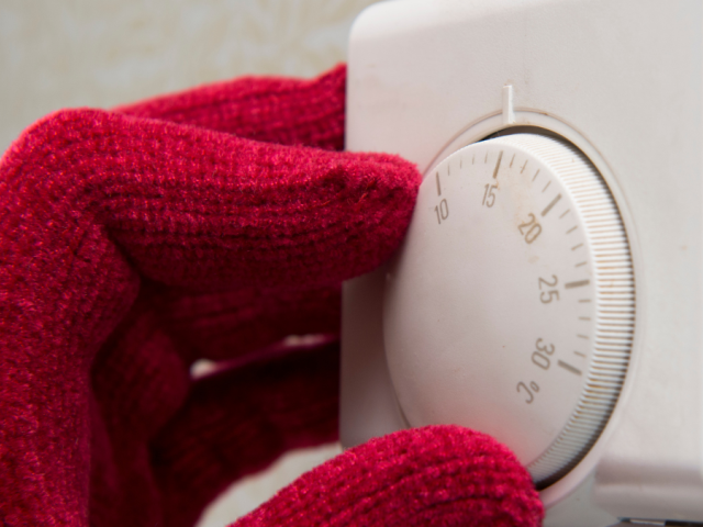 Hand in a red glove turning down a thermostat