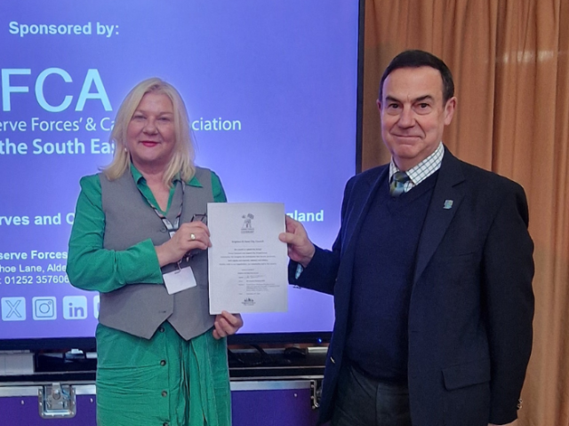 The image shows Cllr Amanda Grimshaw and CE Col (Retd) Patrick Crowley MBE DL holding the Armed Forces Covenant and smiling into camera.