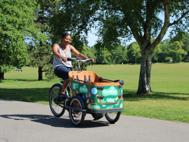 a person riding an ecargo bike on a cycle path with a park in the background
