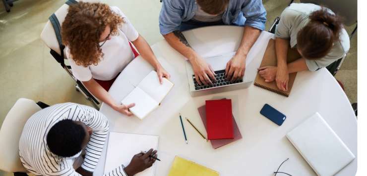 Four people seen from above, sat around a circular table, working.