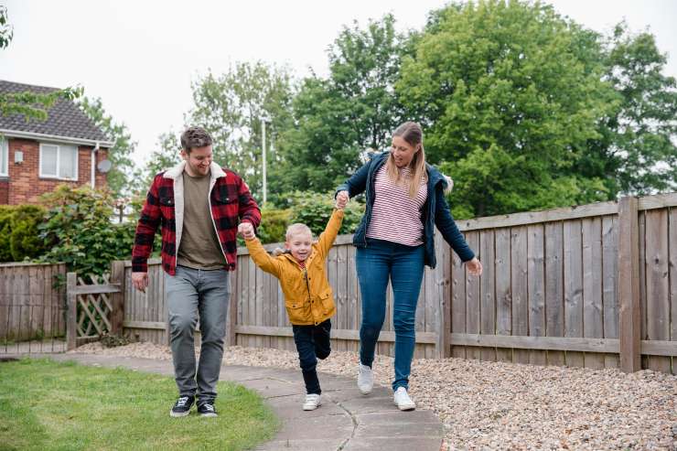 Two adults walking in a garden and playfully lifting a small child