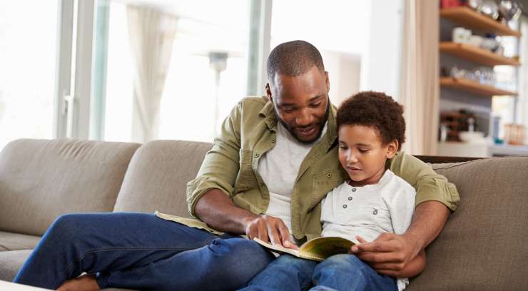 Adult and child sitting on a sofa in a lounge room, reading a book