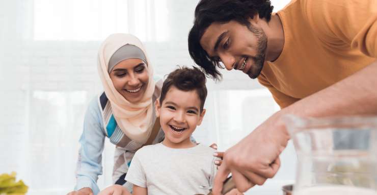 2 adults and a young child smiling. One of the adults is cuttings pizza with a pizza cutter