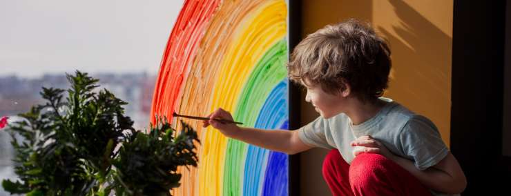 child painting a rainbow on a window