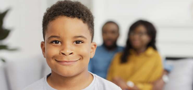 child smiling. Adults out of focus in the background sitting on a sofa