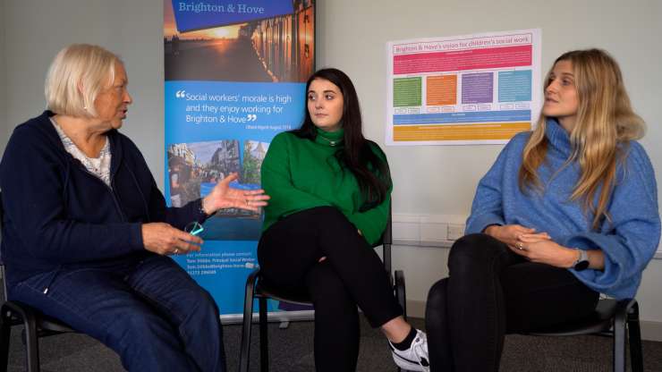 3 people sat on chairs facing the camera, they are having a conversation. There are Brighton & Hove City Council posters on the wall behind them.