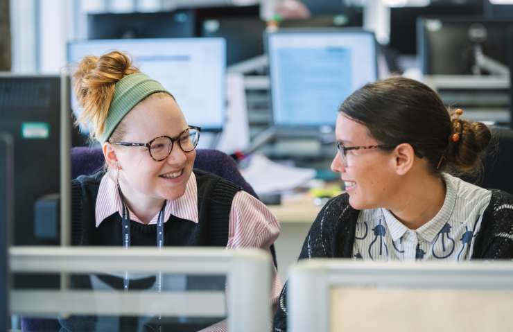 Two people smiling at each other and working together at a bank of computers in an office