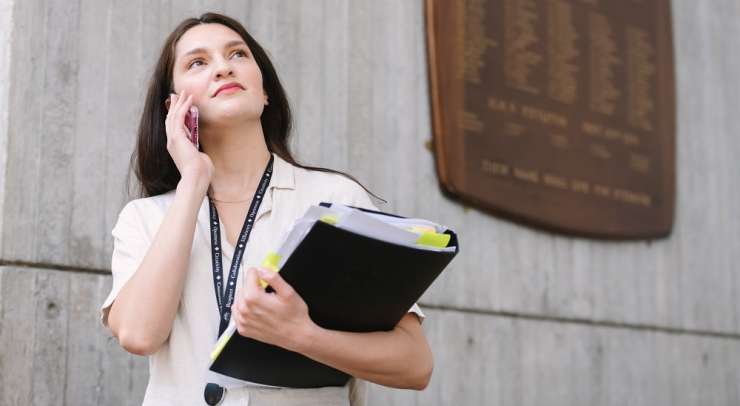 Person on the phone, holding a folder of documents standing outside a council building 