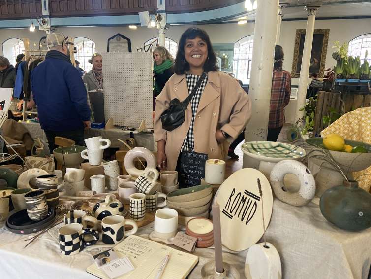 A person standing behind a table which has ceramics displayed from their business Romud Ceramics.